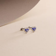 Heart-shaped earrings with blue evil eye design on a beige background