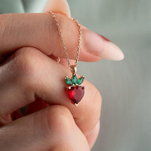 Rose gold necklace with a red and green heart-shaped pendant held by a hand.