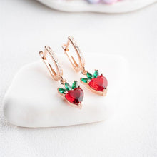 Heart-shaped earrings with red stones and rose gold accents on a white surface
