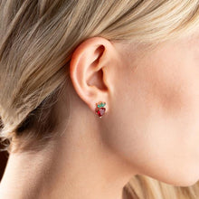 Close-up of an ear wearing a red heart-shaped earring with green leaves.