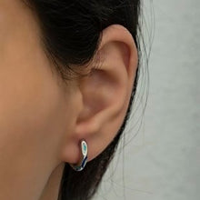 Close-up of an ear wearing a silver earring with a light green gemstone on a neutral background