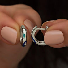 Close-up of a person holding two silver hoop earrings with blue and green accents.