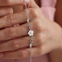Silver bracelet with floral design held by a hand against a pink background