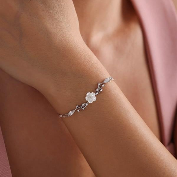 Silver bracelet with floral design on a wrist against a soft pink background