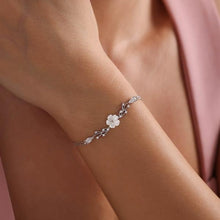Silver bracelet with floral design on a wrist against a soft pink background