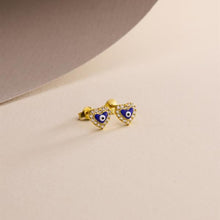 Heart-shaped earrings with blue evil eye design on a beige background