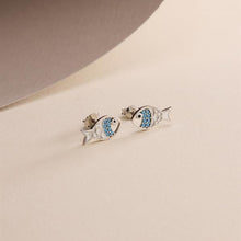 Fish-shaped earrings with blue stones on a beige background