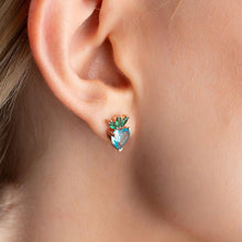 Close-up of an ear wearing a heart-shaped green and blue earring.