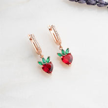 Rose gold earrings with red and green gemstones on a white background