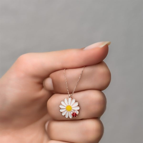 Hand holding a necklace with a daisy pendant against a gray background