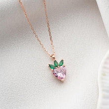 Heart-shaped pink gemstone necklace with green accents on a light gray background