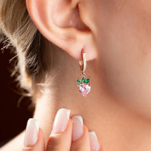 Close-up of a person wearing a heart-shaped earring with green leaves and pink gemstone.