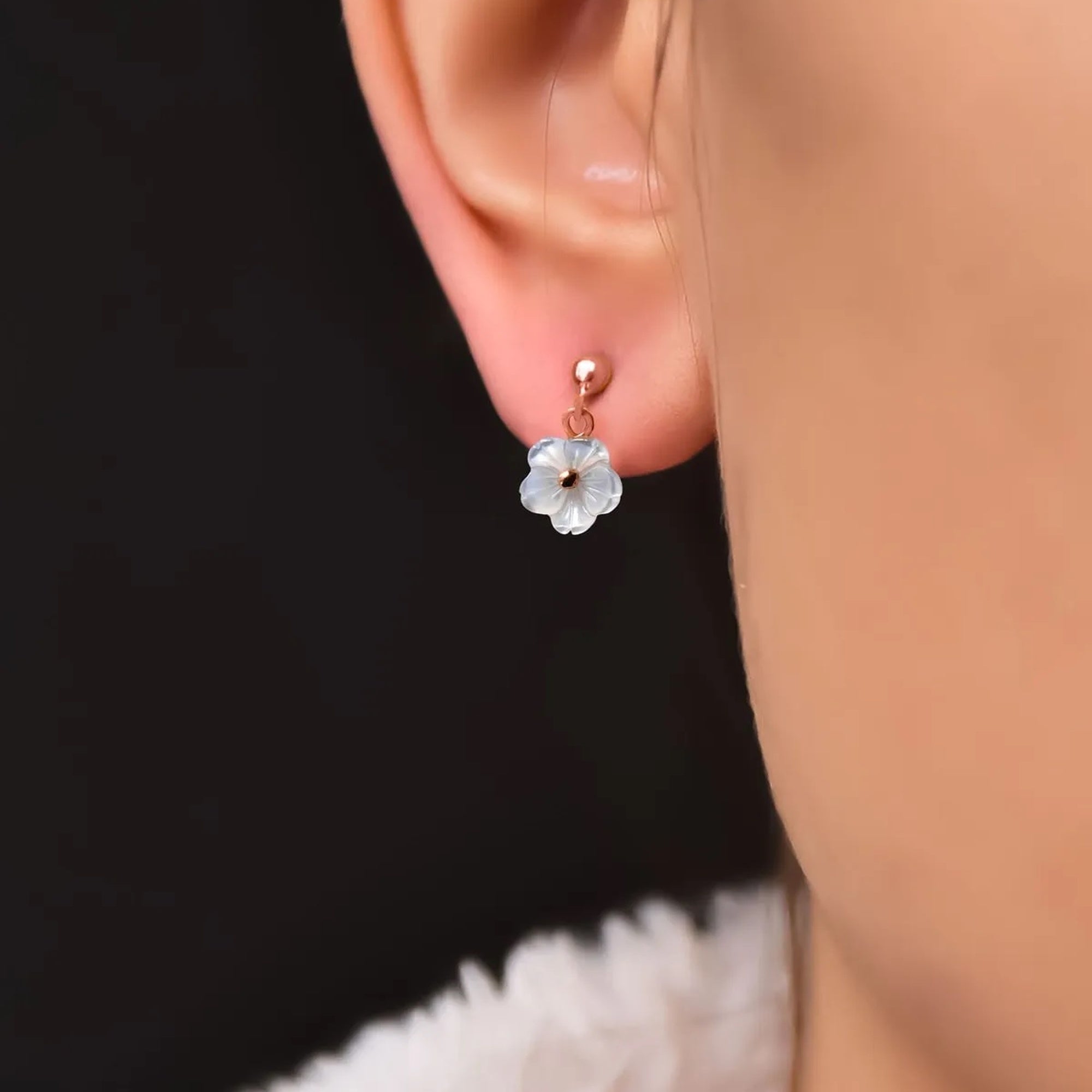 Flower-shaped earring worn on an ear with a black background