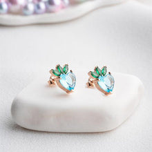 Pair of earrings with green and blue gemstones on a white stone surface