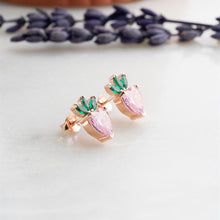 Pair of rose gold earrings with pink and green gemstones on a light background