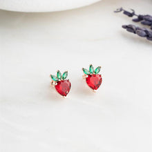 Red heart-shaped earrings with green accents on a white surface