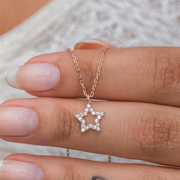 Star-shaped diamond necklace on a finger against a neutral background