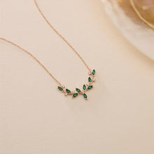 Rose gold necklace with green gemstones on a beige background