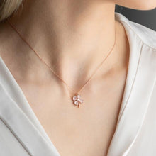 Rose gold necklace with a delicate pendant worn by a person in a white outfit.