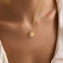 Gold necklace with a flower pendant on a person wearing a white shirt.