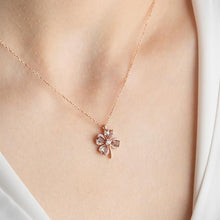 Rose gold necklace with a floral pendant on a person wearing a white top.