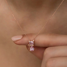 Rose gold necklace with a pink teardrop pendant held by a hand against a beige background