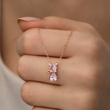 Rose gold necklace with pink teardrop pendant on a hand against a neutral background
