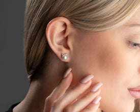 Close-up of a woman wearing a silver earring with a cat design on a neutral background