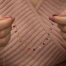 Necklace with colorful heart-shaped pendants held by hands against a textured pink background