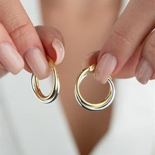 Gold hoop earrings held between two fingers against a neutral background