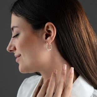 Woman wearing a silver hoop earring with a neutral background