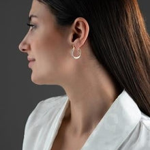 Woman wearing silver hoop earrings against a dark background