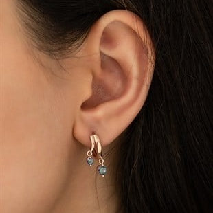 Close-up of an ear wearing a rose gold hoop earring with blue gemstones.