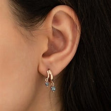 Close-up of an ear wearing a rose gold hoop earring with blue gemstones.