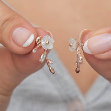Rose gold floral earrings held between fingers against a neutral background