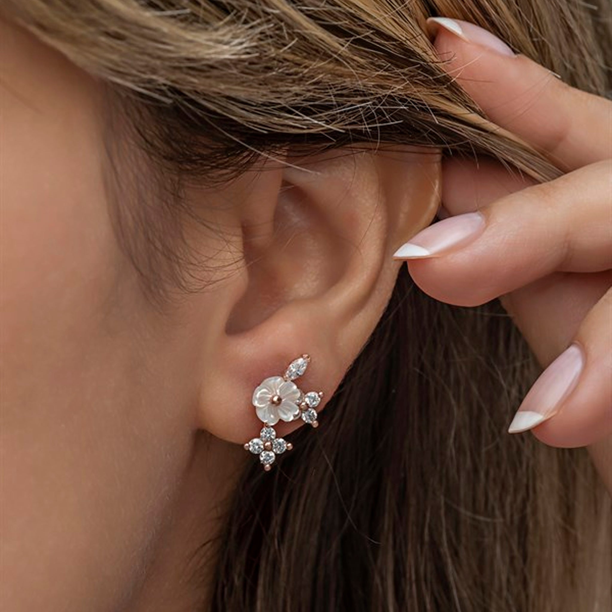 Close-up of a woman wearing a floral earring with a hand adjusting her hair.