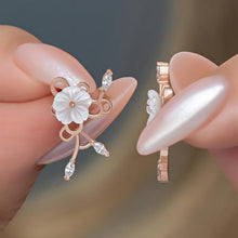 Rose gold earrings with floral design held between fingers against a blurred background