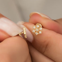 Gold heart-shaped earring being held between fingers with a neutral background