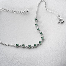 Silver bracelet with green gemstones on a light gray background