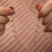 Rose gold necklace with heart-shaped pendants held by hands against a textured pink background