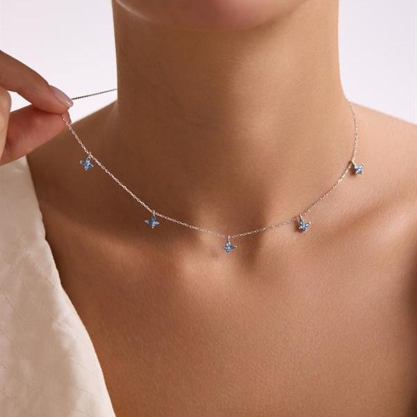 Necklace with blue pendant being adjusted on a person's neck against a neutral background