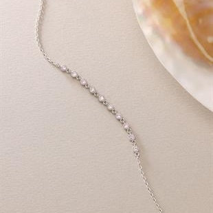 Silver necklace on a light beige surface with a shell in the background