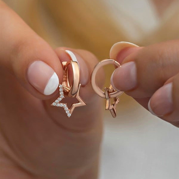 Rose gold earrings with star and moon designs held between fingers against a blurred background
