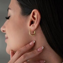 Close-up of a person wearing gold hoop earrings with a neutral background