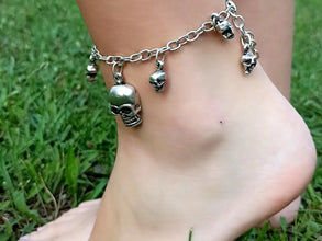 Silver anklet with skull charms on a foot against a grass background