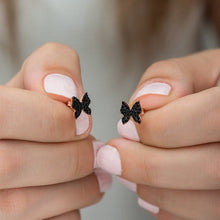 Black bow-shaped earrings held between fingers with a blurred background