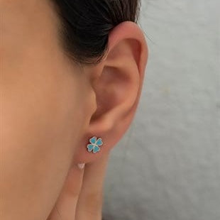 Close-up of an ear wearing a blue flower-shaped earring with a neutral background