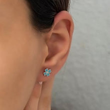 Close-up of an ear wearing a blue flower-shaped earring with a neutral background