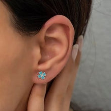 Close-up of an ear wearing a turquoise flower-shaped earring with a neutral background.