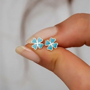 Flower-shaped earrings held between fingers against a neutral background